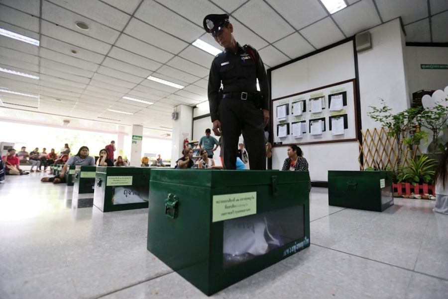 Một cảnh sát đứng coi giữa lúc các tình nguyện viên kiểm tra hòm phiếu. Ảnh: Reuters 