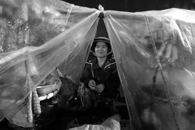 Bà Thanh nép mình bên trong gánh hàng rong được che chắn bởi nilon để tránh gió.