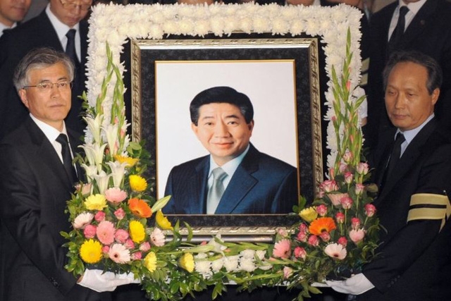 Ông Moon sau đó vẫn không cảm thấy thực sự đam mê chính trị và vẫn muốn làm việc như một luật sư. Ông chỉ thực sự thay đổi suy nghĩ và bắt đầu tham gia chính trường sau vụ tự sát của ông Roh tại một vách núi năm 2009. “Roh thực sự đã định hình nên cuộc đời tôi. Cuộc sống của tôi sẽ thay đổi rất nhiều nếu không gặp ông ấy. Ông ấy chính là vận mệnh của tôi, ông Moon viết trong hồi ký cá nhân về người bạn thân của mình. Trong ảnh: Ông Moon Jae-in (trái) nâng di ảnh của tổng thống Roh Moo Hyun trong lễ tang năm 2009 (Ảnh: BBC)